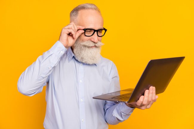 Photo of concentrated old charming man look laptop smile wear glasses isolated on yellow color background