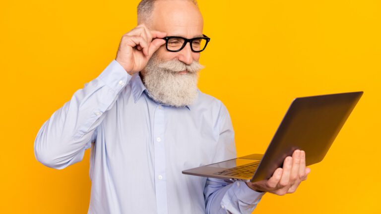 Photo of concentrated old charming man look laptop smile wear glasses isolated on yellow color background
